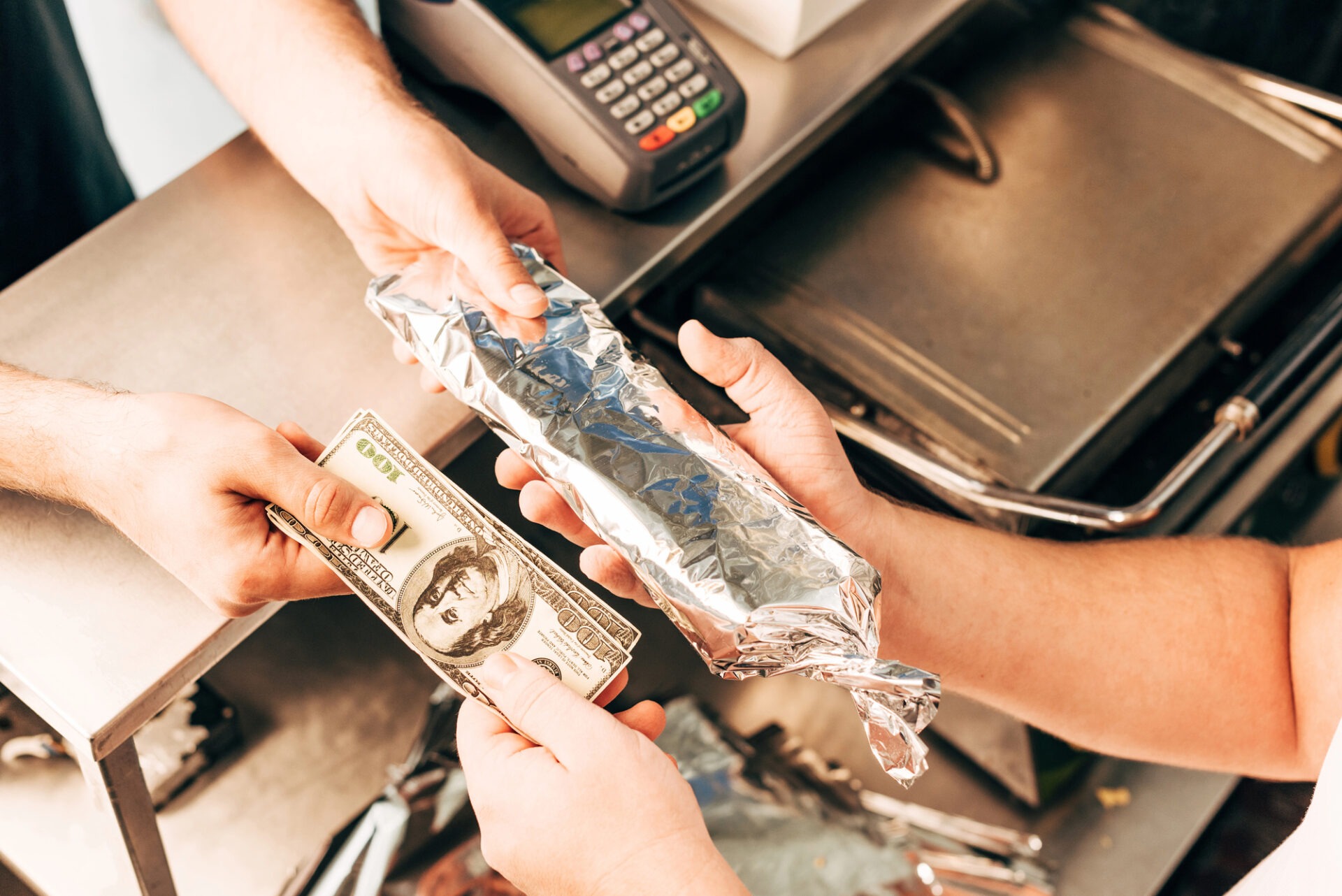 Klant betaalt met een 100 dollarbiljet voor in zilverfolie verpakt eten aan een balie met een pinapparaat.