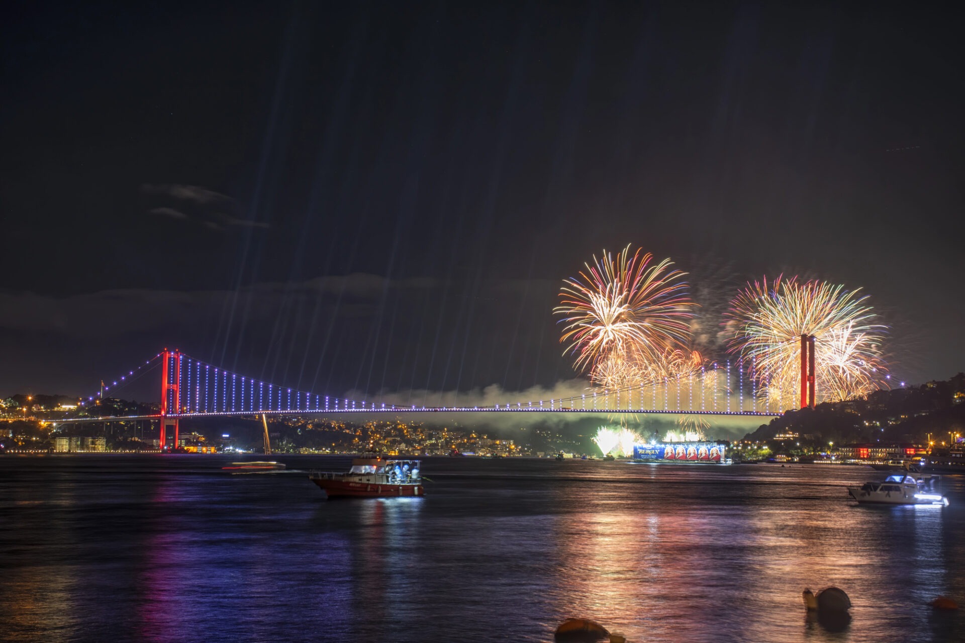 Spectaculair vuurwerk en lichtstralen boven het water naast de rood verlichte Bosporusbrug in de nacht.